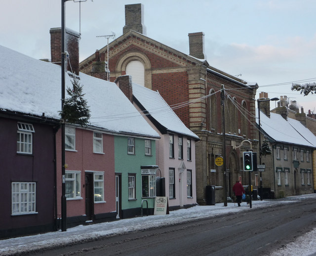 High Street, Needham Market Beyond the colourful houses, the large building houses a charity shop and a variety of small antiques business. Immediately beyond is the turn for The Causeway at the edge of the square.