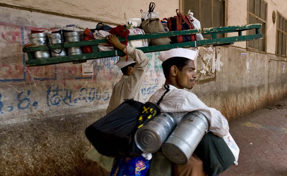 The famous Dabbawala or Tiffin Wallahs of Mumbai... Tiffin Wallah translates as one who carries the box. Tiffin is an old English word for a light lunch, and also the name of the multi-compartment metal lunch box that carries it. The Tiffin Wallah originated over a century ago when the many Indians working for British companies disliked the food served at work. Tiffin service was created to bring home cooking to the workplace. Today the city's 5,000 tiffin-wallahs deliver 200,000 tiffin-boxes fi
